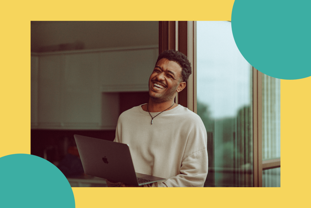 A man is working from home, smiling at his laptop computer.