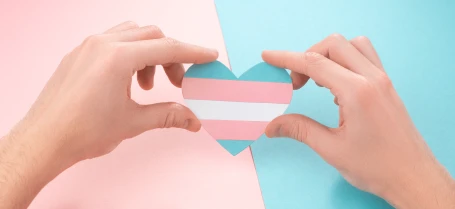 hands holding a paper heart cutout of the transgender flag